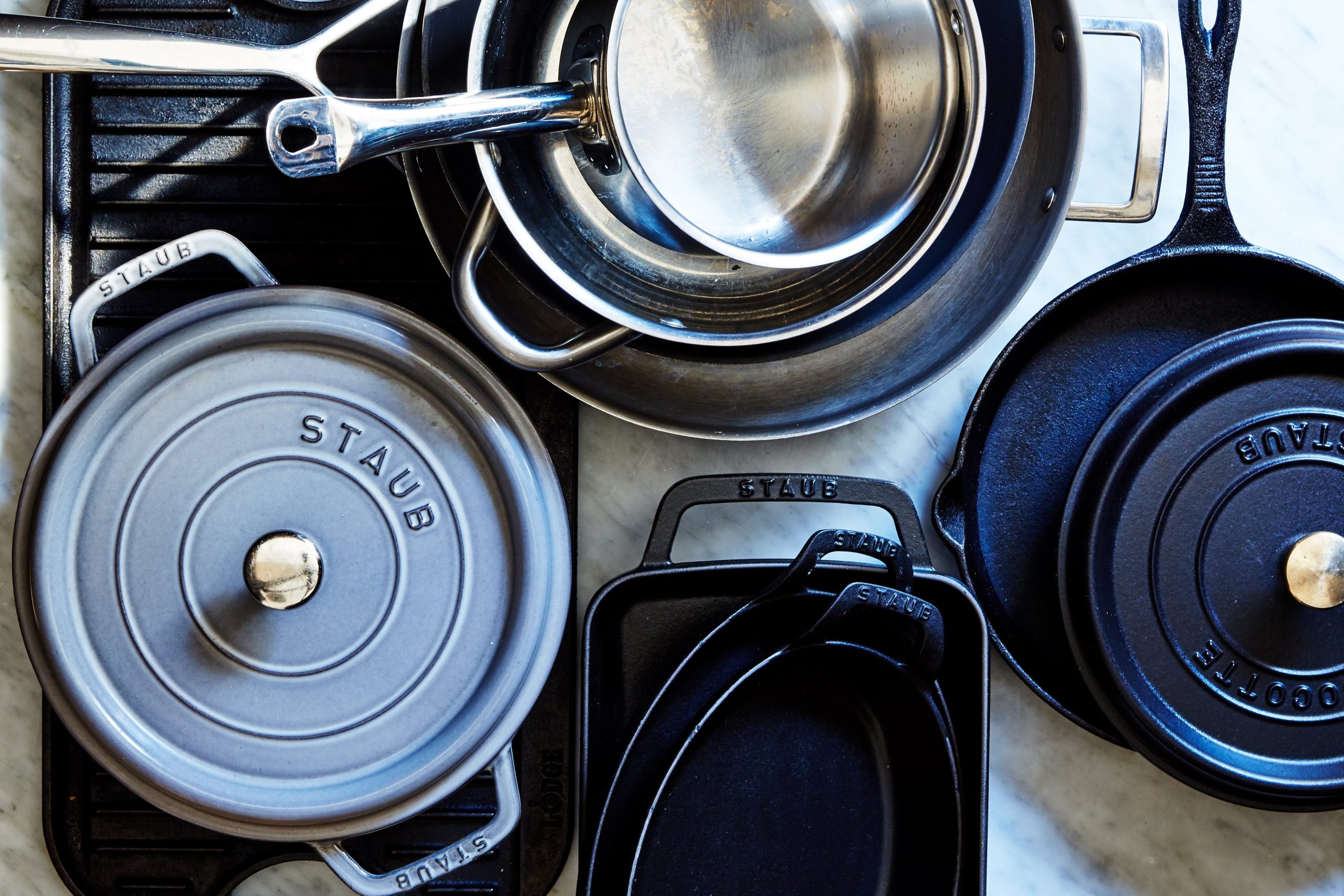 overhead shot of many stainless steel and cast iron pots, pans, and dutch ovens on a stove