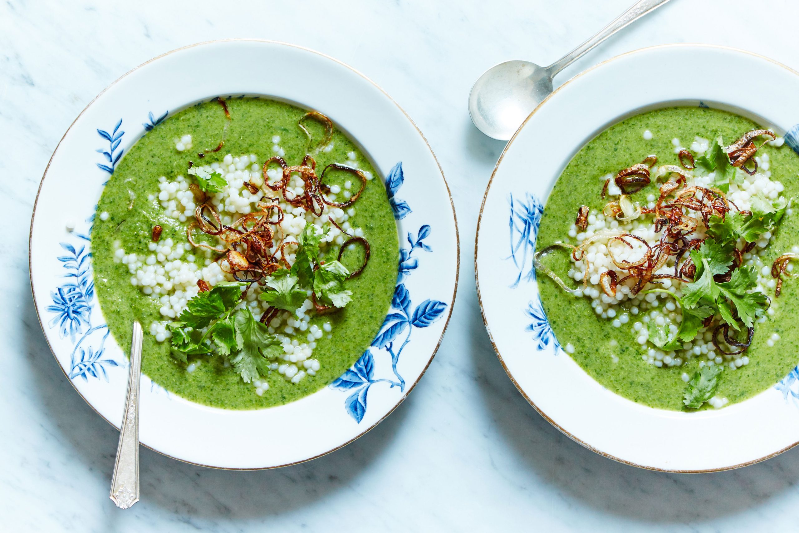 Vegan Broccoli Coconut Soup with Spinach and Crispy Shallots served in two plates with spoons against a marble background