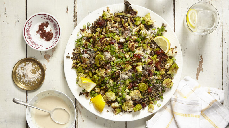 Hearty salad with lentils and roasted vegetables and lemon wedges on a large white platter against a white wooden background